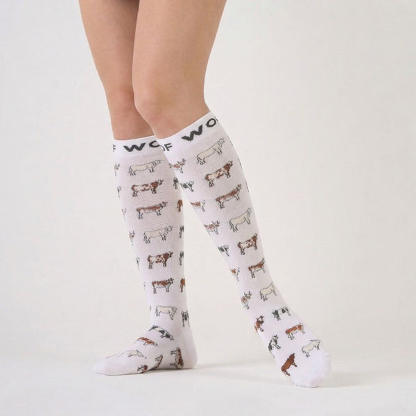 Nurse wearing white knee-high compression socks printed with cute, illustrated cows and top cuff branding.