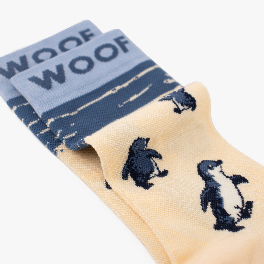 Folded view showing cute penguin illustration on cream bamboo crew compression socks with penguin design.