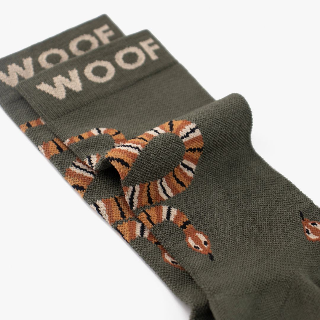 Folded view showing slithering snake illustration on olive green bamboo crew compression socks with snake design.